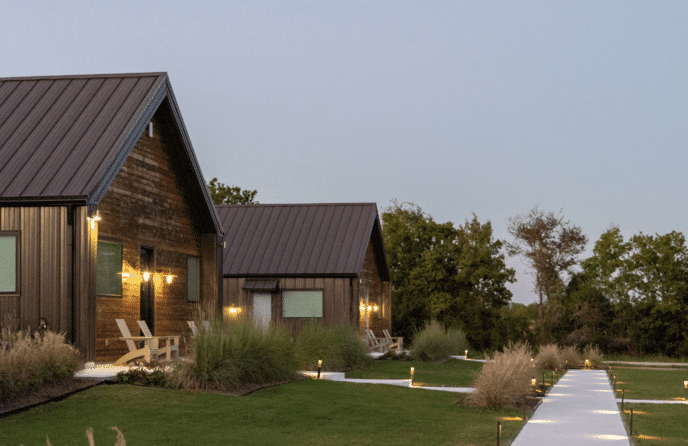 Evening view of round top vacation rental - The Retreats at Element Ranch in Round Top, Texas, featuring modern rustic cabins with warm outdoor lighting, lush landscaping, and a peaceful walking path.